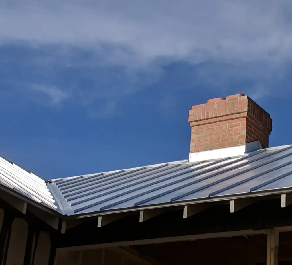 Standing seam metal roof on a cabin with a brick chimney